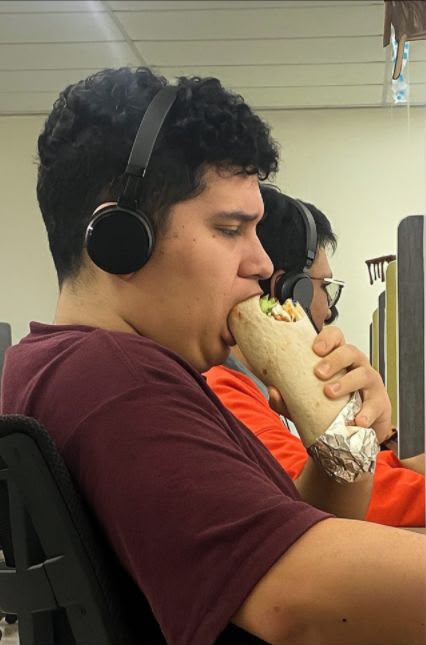 El beneficiario con audífonos, mordiendo un burrito enorme en su escritorio
