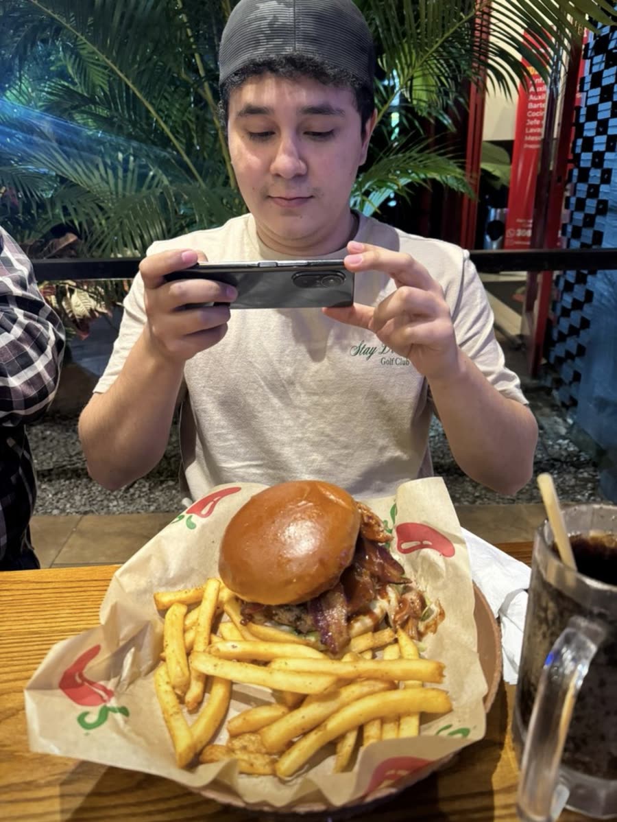 El beneficiario tomándole foto con su celular a una hamburguesa con papas fritas